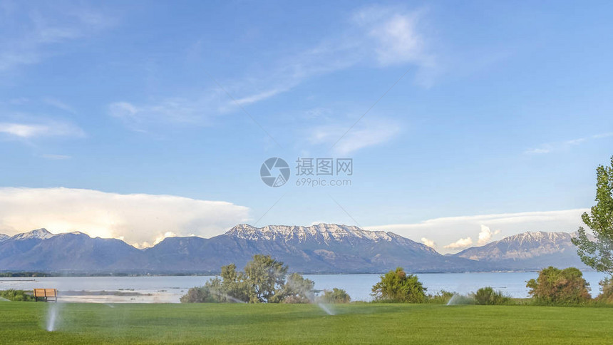 Pano框架与洒水器的绿色草地和湖景和白雪皑的山自动灌溉系统与风景如画的自然图片