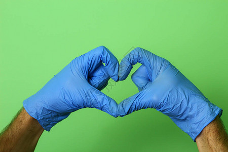 握着医疗手套的手展示了绿色背景上的心脏姿态图片