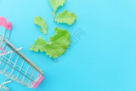 生态产品保健食品素食概念小型超市杂货推车购物与绿色生菜叶隔离在蓝色柔和的彩色背图片