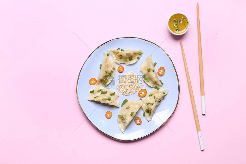 颜色背景上带有美味日本饺子和酱汁的盘子图片