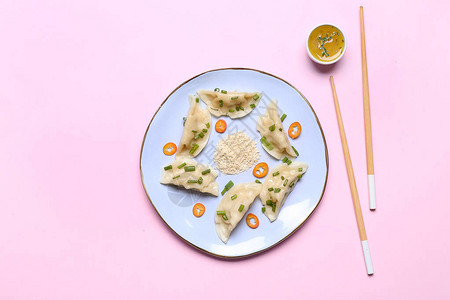 颜色背景上带有美味日本饺子和酱汁的盘子图片