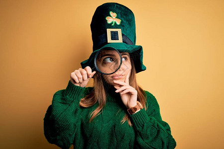 穿着绿色帽子的漂亮女人在圣徒节上拿着放大玻璃庆祝严肃的面孔思考问题图片