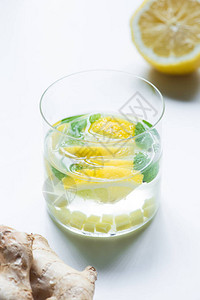 白底柠檬和姜根附近玻璃杯中新鲜柠檬图片