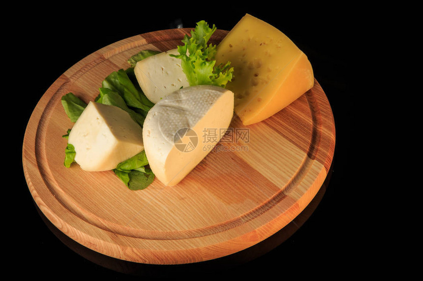 黑背景圆木板绿色沙拉叶上各种硬奶酪图片