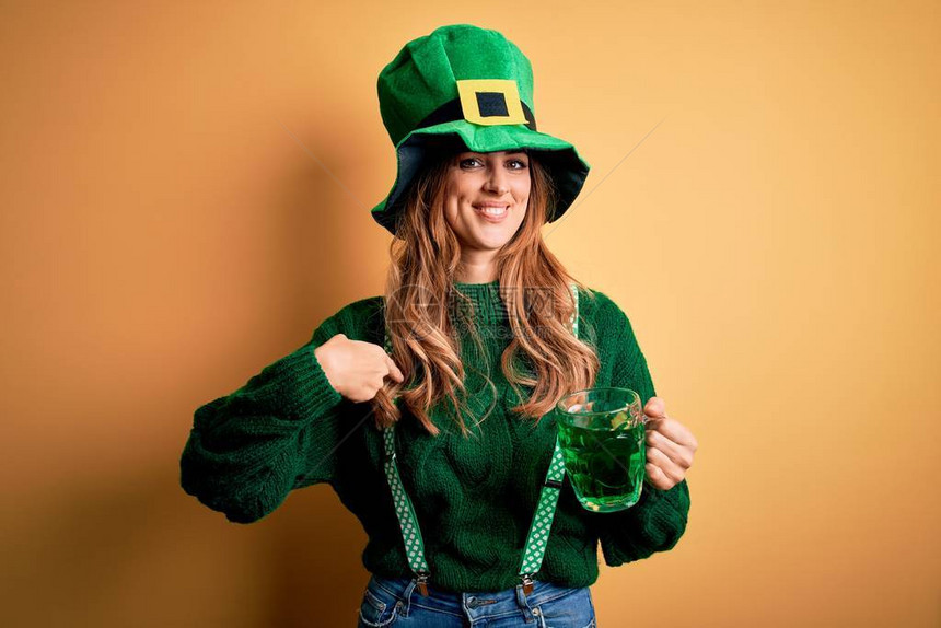 美丽的女人戴着帽子喝着绿色饮料罐庆祝圣帕特里克节图片