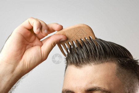 特写男人用灰色背景上的木梳理头发治疗脱发和头皮屑概念男士化妆品图片