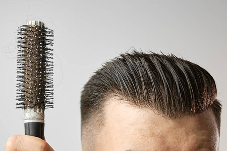 男子使用圆刷为他的头发造型理发店后在家进行头发护理在白色背景上图片
