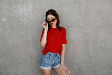 身穿空白红色T恤和牛仔短裤的亚洲女潮人靠在粗糙的街墙上摆姿势图片