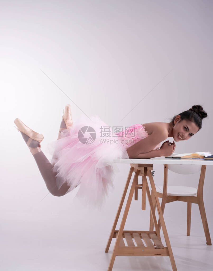 身穿粉红色芭蕾舞服的年轻美女躺在木制桌子上抬起脚趾面带微笑的图片