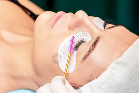 美容师在美容院延长眼睫毛手术期间使用眼电刷图片