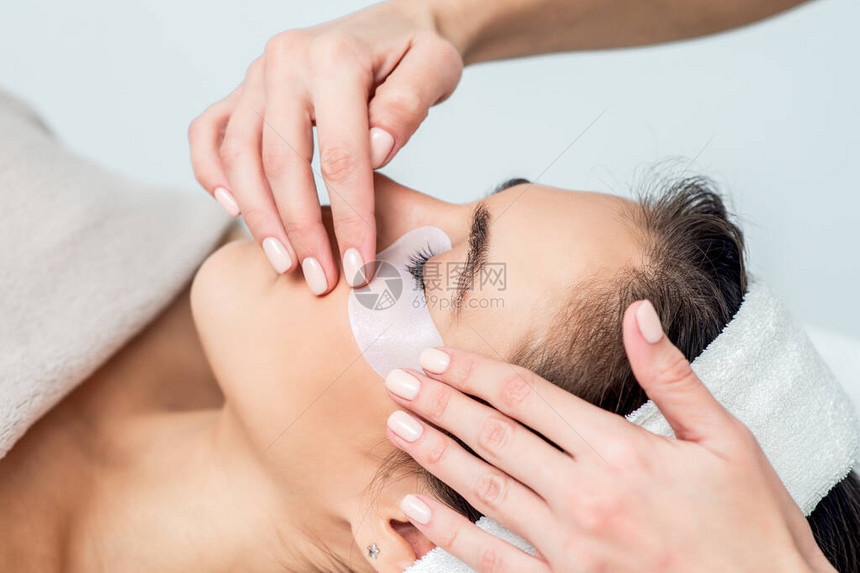 美容师的手把丝带放在年轻女眼皮下在眼睫毛延伸图片