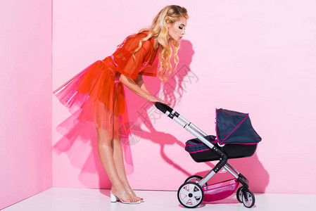 美丽的女孩婴儿车用粉红色的洋娃图片