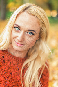美丽的年轻金发美女的肖像在秋天公园看摄影机时图片