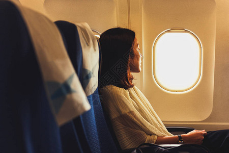坐在飞机上的旅行者女人透过窗户向外看图片