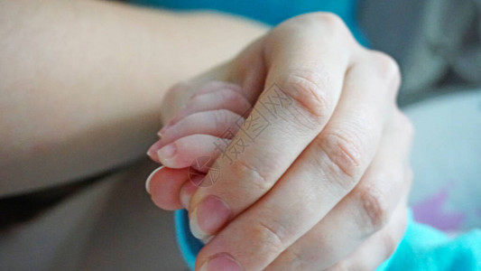 一个新生儿的指甲是用特殊的婴儿剪刀的一只成人手握着一只小孩子的手母亲小心翼地给女儿剪指甲一个在茧家庭环境中背景图片