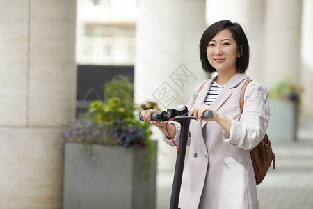 骑着电动摩托车的亚洲女在城市街上摆姿势图片