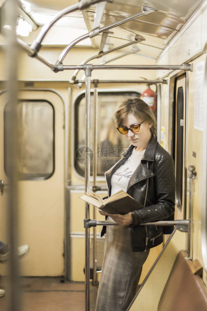 地铁车厢的女商人读一本书戴着墨镜的漂亮女孩和地铁车里的夹克时尚又时尚的女图片
