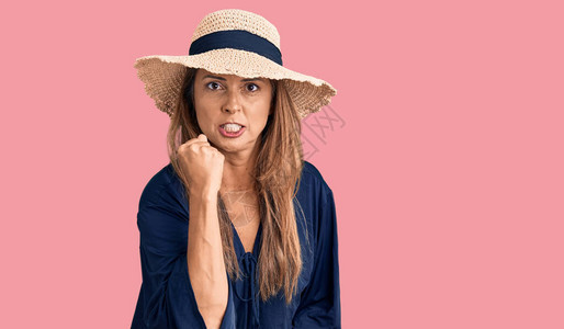 穿着暑期帽子的中年西班牙妇女愤怒而疯狂地举起拳头感到沮丧和愤怒图片