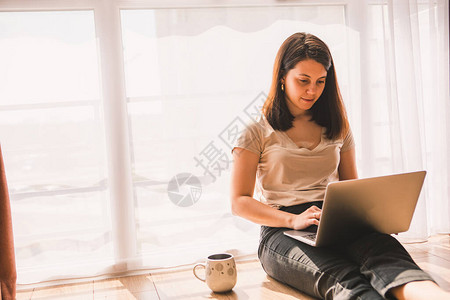 女人坐在地板上在大窗户附近的笔记本电脑上工作自我隔离隔图片