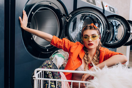 时髦的妇女在洗衣店用洗衣机附近穿着衣物图片