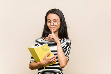 年轻亚洲女学生持有一本书保守秘密或要求保持沉默图片
