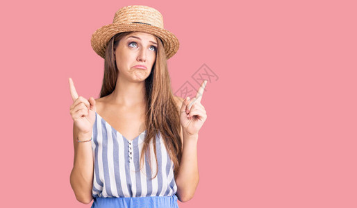 穿着暑假帽子的年轻金发美女抬头看着悲伤和不安指向方时用手指图片