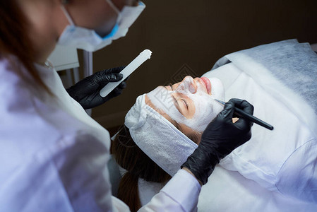 在女孩脸上涂抹脱皮gommage在美容院进行皮肤清洁手术时图片