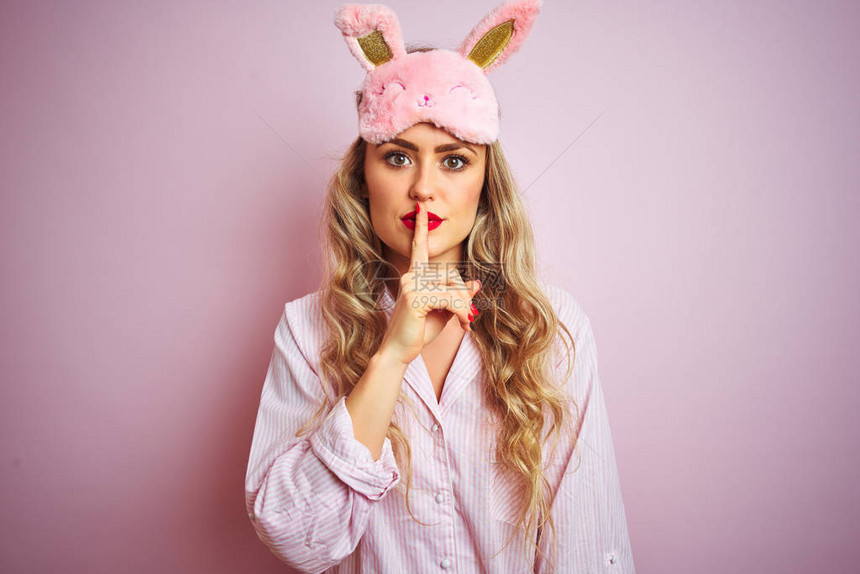 穿着睡衣的年轻美女在粉红色孤立的背景上戴着睡面具图片