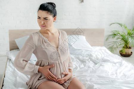 睡衣中身着焦虑的孕妇在床上感觉疼痛图片