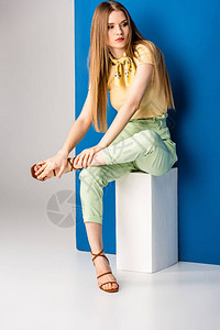 穿着绿色夏季长裤的时尚女和坐在灰色和蓝色白立方体图片