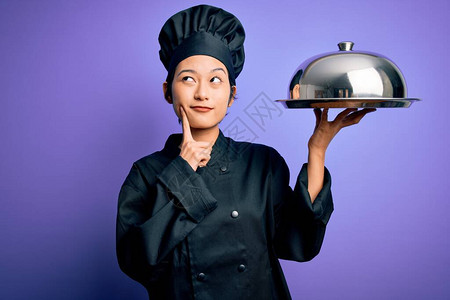 年轻漂亮的厨师女人穿着炊具制服和帽子拿着托盘图片