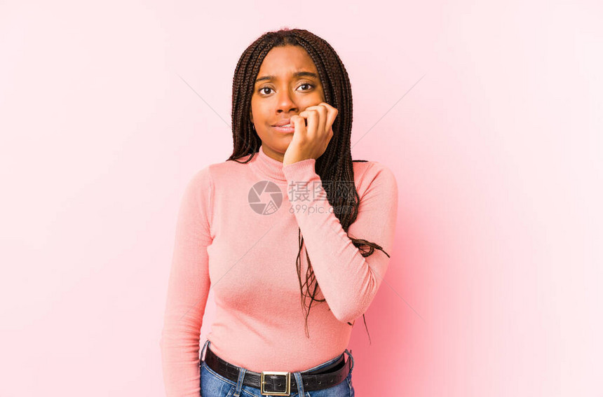 年轻非裔美国妇女被困在粉红色背景的咬指甲上神经紧图片
