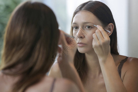 年轻caucasian女人在镜子前用血清做眉毛和睫毛生长图片