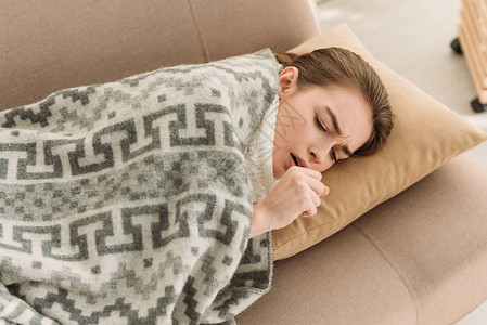 生病的女孩躺在毯子下的沙发上咳嗽图片