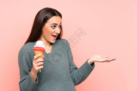 年轻女人拿着玉米角冰淇淋孤立在粉红背景上面部图片