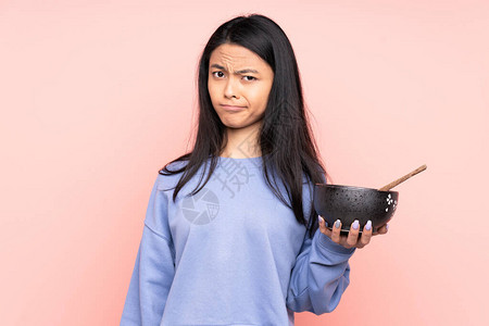 年轻亚裔女在吃着一碗面条和筷子时图片