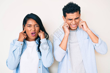 穿着便衣用指头遮住耳朵的美丽的拉丁年轻夫妇对响亮音乐的吵闹声表示不满图片