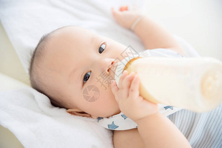 亚洲小孩在床上用奶瓶喝牛奶图片