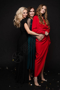 演播室全长肖像三名美丽的年轻女士穿着晚礼服装扮成摄影机黑色背景新年晚图片