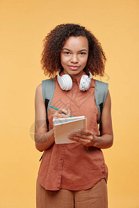 带无线耳机的非裔美国女学生在笔记板制片厂拍摄时写下课堂图片