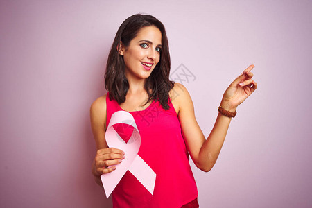 年轻美丽的女士在粉红的孤立背景上带着癌症丝带快乐地用手和图片