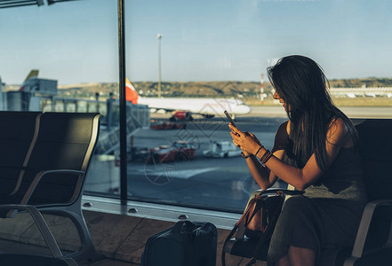 一位女旅客坐在机场等待航班时使用手机图片