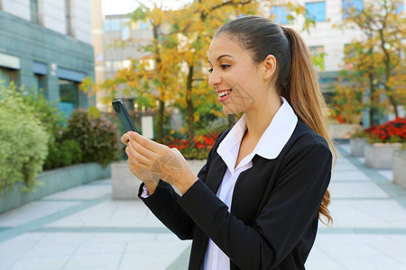 正面的年轻女商人用她的智能电话应用程序和城市背景发来照片图片
