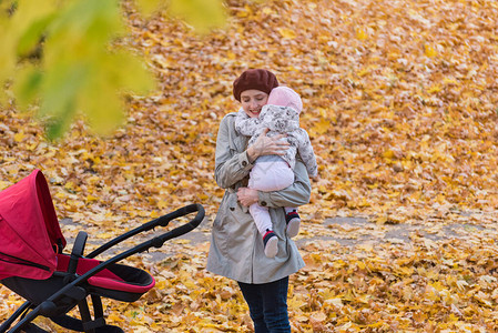 年轻的母亲在秋天的公园里抱着她的孩子母亲带着婴儿车走在图片