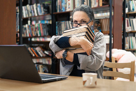 一个女人在图书馆找书一位中年妇女看着书架上的一本书她研究新图片