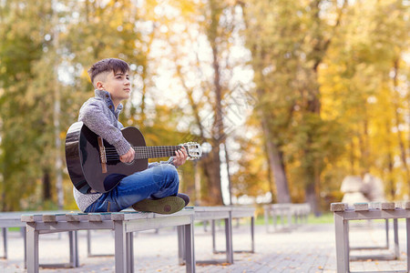 一个青少年街头音乐家在公园的秋天弹着图片