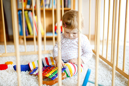 美丽的小女婴站在围栏里面可爱的孩子在玩五颜六色的玩具或托儿所图片