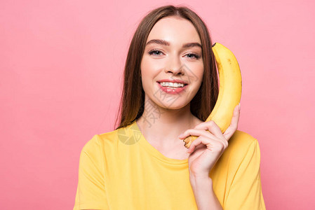 迷人的微笑女孩拿着香蕉看着被粉红图片