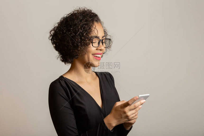 微笑的年轻非洲裔美国女人戴着眼镜看手机的正面肖像美丽的年轻女孩卷曲的头发使用她的智能手机与朋友聊天图片