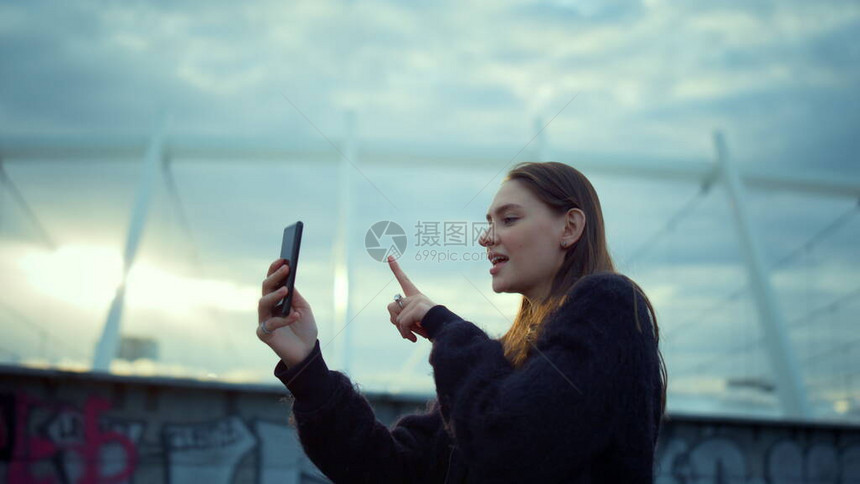 积极的女孩在手机上为城市的博客制作自我视频快乐的女孩在智能手机上在线视频通话现代博主在手机上拍摄视频年轻女子在外面的手机摄图片
